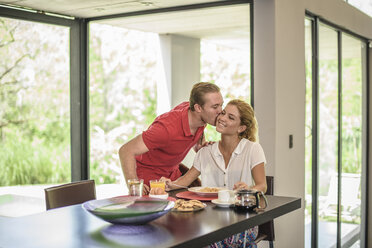 Man kissing girlfriend on cheek at breakfast table - ISF10355