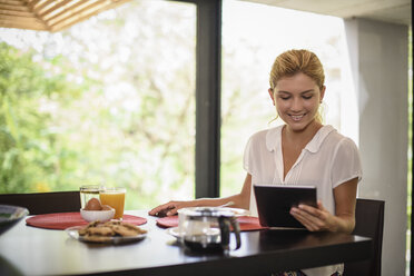 Junge Frau am Frühstückstisch mit digitalem Tablet - ISF10356