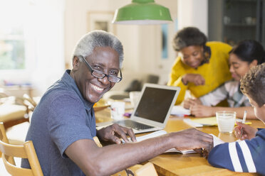 Porträt eines lächelnden, selbstbewussten älteren Mannes, der mit seiner Familie einen Laptop benutzt - CAIF20685