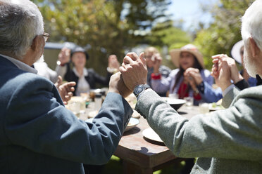 Aktive ältere Freunde halten sich an den Händen und beten am sonnigen Tisch einer Gartenparty - CAIF20706