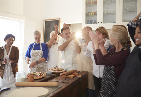 Koch und aktive Seniorenfreunde klatschen beim Pizza-Kochkurs, lizenzfreies Stockfoto