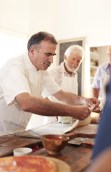 Focused chef spreading pizza dough in cooking class - CAIF20712