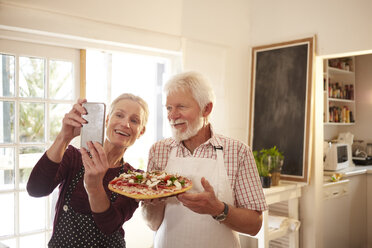 Smiling, confident senior couple taking selfie with pizza at cooking class - CAIF20717