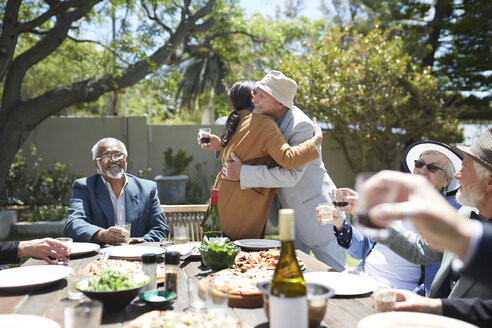 Freunde stoßen bei einem sonnigen Gartenfest auf ein sich umarmendes älteres Paar an - CAIF20729