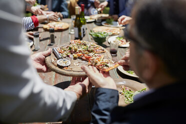 Freunde teilen sich eine selbstgemachte Pizza am sonnigen Terrassentisch - CAIF20731