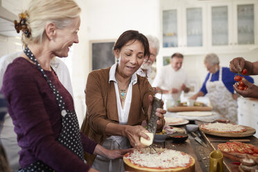 Ältere Freundinnen reiben im Kochkurs Käse über Pizza - CAIF20738