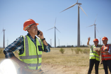 Smiling engineer talking on cell phone at sunny wind turbine power plant - CAIF20752