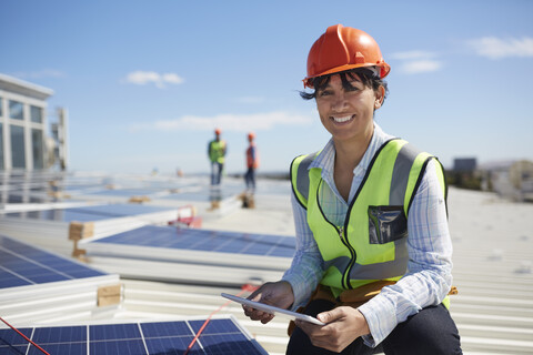 Porträt einer lächelnden, selbstbewussten Ingenieurin mit digitalem Tablet, die Solarzellen in einem sonnigen Kraftwerk überprüft, lizenzfreies Stockfoto