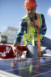 Männlicher Ingenieur mit Walkie-Talkie bei der Reparatur eines Solarpanels im Kraftwerk - CAIF20755