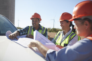 Engineers reviewing blueprints on truck at sunny wind turbine power plant - CAIF20769