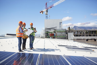 Ingenieure mit Bauplan für Solarzellen in einem sonnigen Kraftwerk - CAIF20775