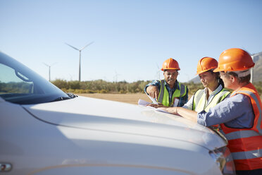 Ingenieure begutachten den Bauplan auf einem LKW in einem sonnigen Windkraftwerk - CAIF20782