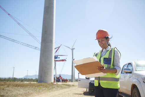 Lächelnde Ingenieurin mit Bauplan in einem sonnigen Windkraftwerk - CAIF20786