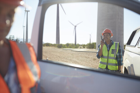 Lächelnder Ingenieur mit Walkie-Talkie an einem Lastwagen in einem sonnigen Windkraftwerk, lizenzfreies Stockfoto