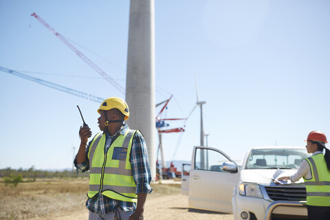 Männlicher Ingenieur mit Walkie-Talkie an einer sonnigen Windkraftanlage, lizenzfreies Stockfoto