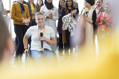 Das Publikum klatscht für eine Sprecherin im Rollstuhl, lizenzfreies Stockfoto