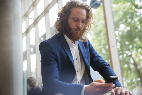 Geschäftsmann, der mit seinem Smartphone in der Büro-Lobby SMS schreibt, lizenzfreies Stockfoto