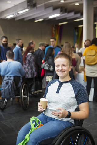 Porträt einer lächelnden, selbstbewussten jungen Frau im Rollstuhl, die auf einer Konferenz Kaffee trinkt, lizenzfreies Stockfoto