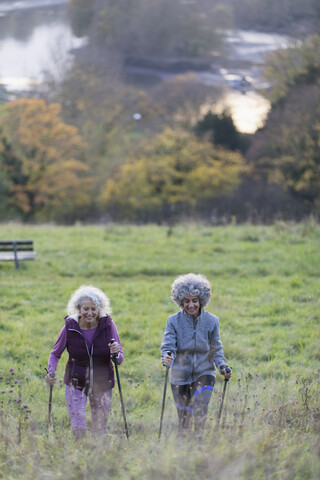 Aktive Seniorinnen, die mit Stöcken auf einen ländlichen Hügel wandern, lizenzfreies Stockfoto