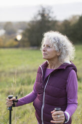 Nachdenkliche aktive ältere Frau beim Wandern mit Stöcken in einem ländlichen Gebiet - CAIF20937