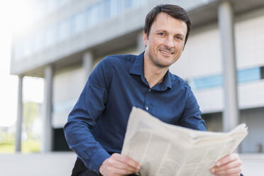 Portrait of smiling businessman with newspaper in the city - DIGF04662