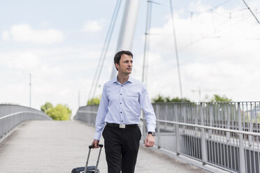 Businessman with rolling suitcase crossing a bridge - DIGF04680