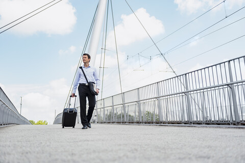 Geschäftsmann mit Rollkoffer beim Überqueren einer Brücke, lizenzfreies Stockfoto