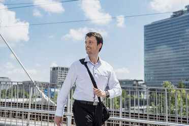 Smiling businessman walking on a bridge - DIGF04686