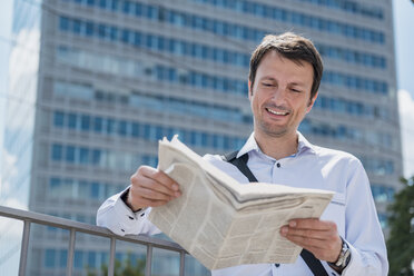 Smiling businessman reading newspaper in the city - DIGF04687