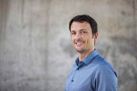 Portrait of smiling businessman in front of concrete wall stock photo