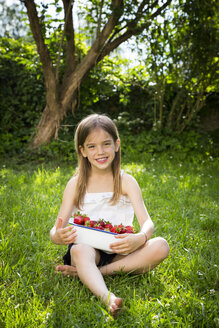 Porträt eines lächelnden kleinen Mädchens auf einer Wiese sitzend mit einer Schale voller Erdbeeren - LVF07099