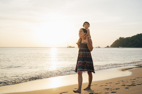 Thailand, Krabi, Koh Lanta, Mutter mit kleiner Tochter auf den Schultern am Strand bei Sonnenuntergang, lizenzfreies Stockfoto