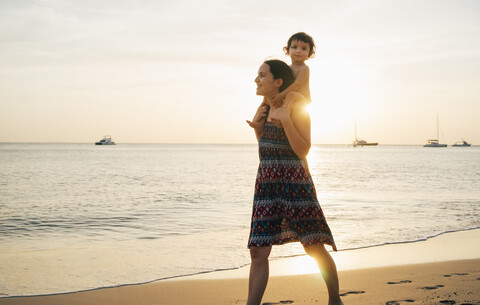 Thailand, Krabi, Koh Lanta, Mother with little daughter on her shoulders on the beach at sunset stock photo