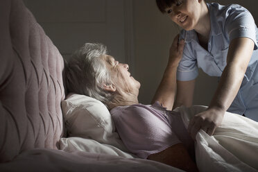Personal care assistant chatting to senior woman in bed - CUF32391