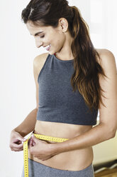 Smiling curvy woman in lingerie measuring abdomen using tape measure  against pink background stock photo