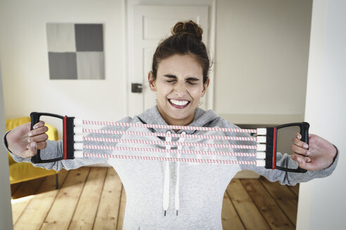 Young woman straining to exercise using chest expander in living room - CUF32615