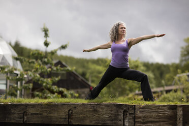 Mature woman practicing warrior pose in eco lodge garden - CUF32622
