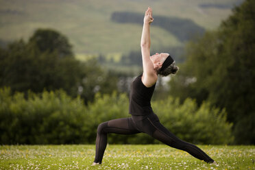 Ältere Frau übt Yoga-Krieger-Pose mit erhobenen Armen im Feld - CUF32627