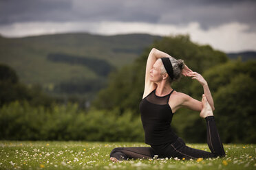 Reife Frau macht Spagat und übt Yoga auf einem Feld - CUF32631
