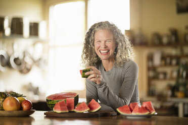 Porträt einer reifen Frau, die in der Küche eine Wassermelone isst - CUF32633
