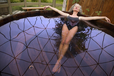 Mature woman lying back in hot tub at eco retreat - CUF32638