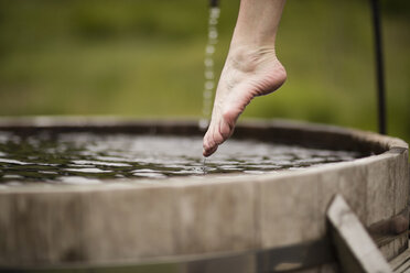 Bare foot of mature woman stepping into fresh cold water tub at eco retreat - CUF32642