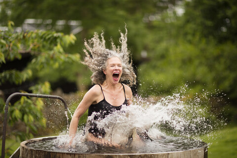Ältere Frau spritzt in frischem kaltem Wasser Wanne auf Öko-Retreat, lizenzfreies Stockfoto