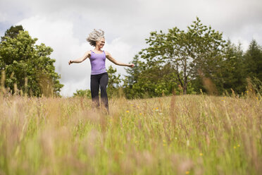 Ältere Frau mit langen grauen Haaren läuft durch ein Feld - CUF32654