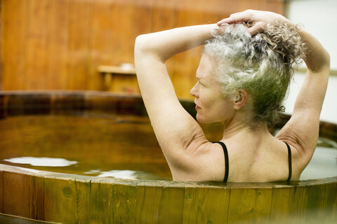 Reife Frau mit Händen in den Haaren im Whirlpool im Öko-Retreat, lizenzfreies Stockfoto