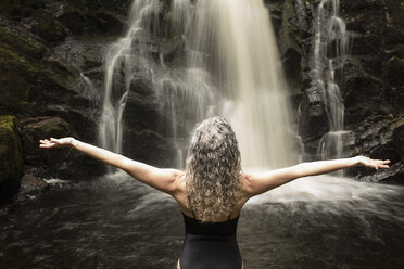 Rückansicht einer reifen Frau, die eine Yoga-Pose vor einem Wasserfall einnimmt - CUF32665
