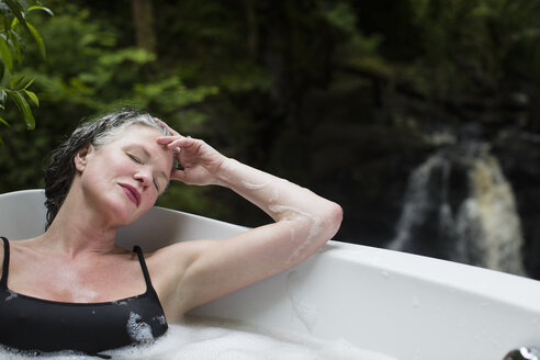 Reife Frau mit geschlossenen Augen im Schaumbad vor einem Wasserfall im Öko-Retreat - CUF32666