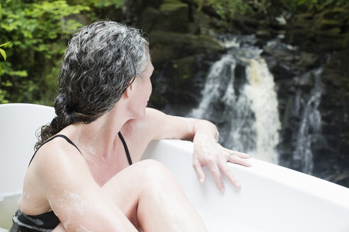 Reife Frau im Schaumbad mit Blick auf den Wasserfall im Öko-Retreat - CUF32669