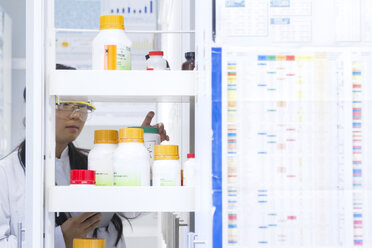 Female scientist selecting specimen jar from shelf in laboratory - CUF32672