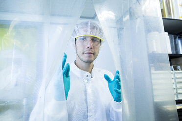 Portrait of male scientist behind plastic curtain in lab cleanroom - CUF32675